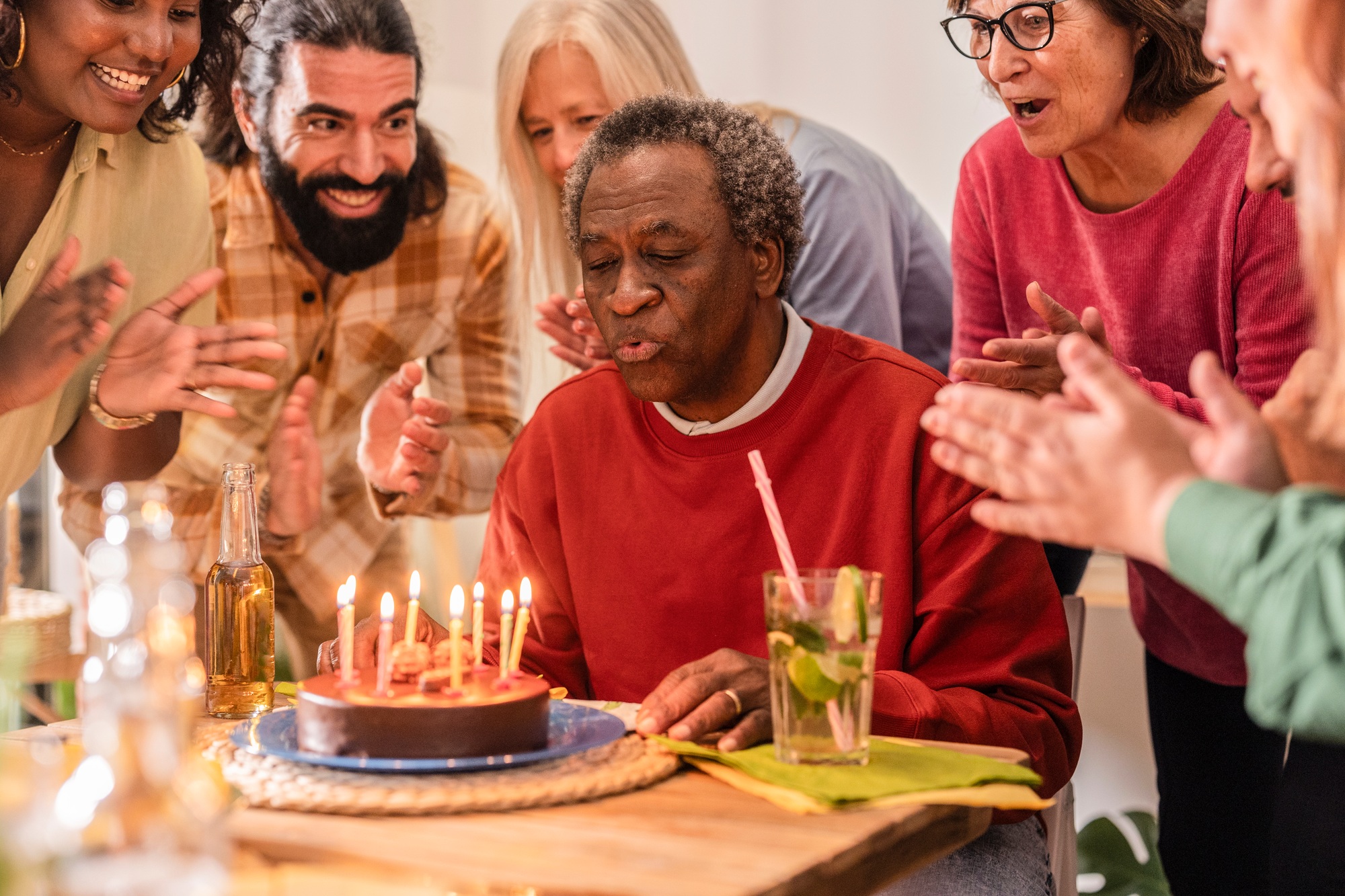 Senior man blowing out candles on birthday cake surrounded by family